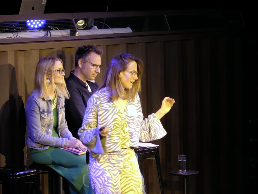 Evi presenting on stage at the Kaluza offsite alongside two seated panellists, leading a session on team mindset